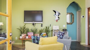 A living room with a flat-screen TV, a couch, a chair, and several potted plants. - Martian Rose - Out Of This World Stargazing Cabin 2 Bedroom Home by RedAwning (Joshua Tree)