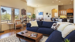 A modern living room with a sectional sofa, a coffee table, and a dining area with a kitchen in the background. - Horizon House Hot Tub, Fire Pit & Bbq Adobe In Jt 4 Bedroom Home by RedAwning (Joshua Tree)