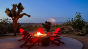 A fire pit with red Adirondack chairs and a view of a desert landscape at dusk. - Horizon House Hot Tub, Fire Pit & Bbq Adobe In Jt 4 Bedroom Home by RedAwning (Joshua Tree)