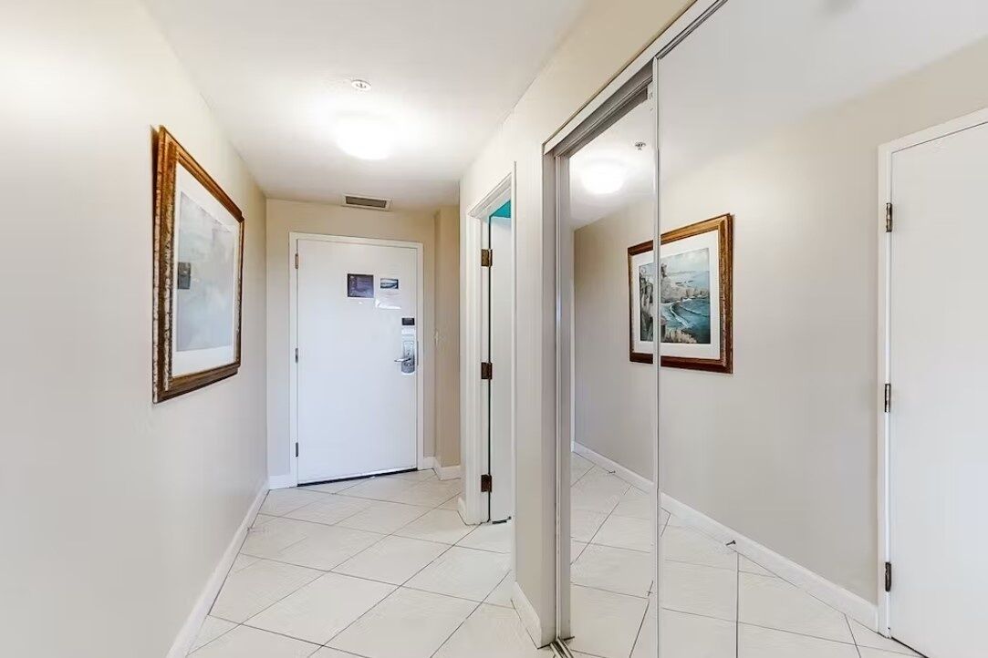 A hallway with a white door, framed pictures on the walls, and a tiled floor.