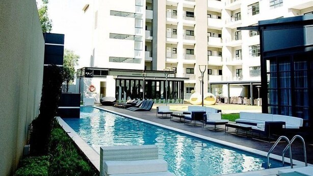 A pool area with lounge chairs and a building in the background. - The Capital 20 West (Johannesburg)