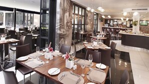 A modern restaurant with multiple dining tables set for guests, a bar area, and large windows offering views. - The Capital 20 West (Johannesburg)