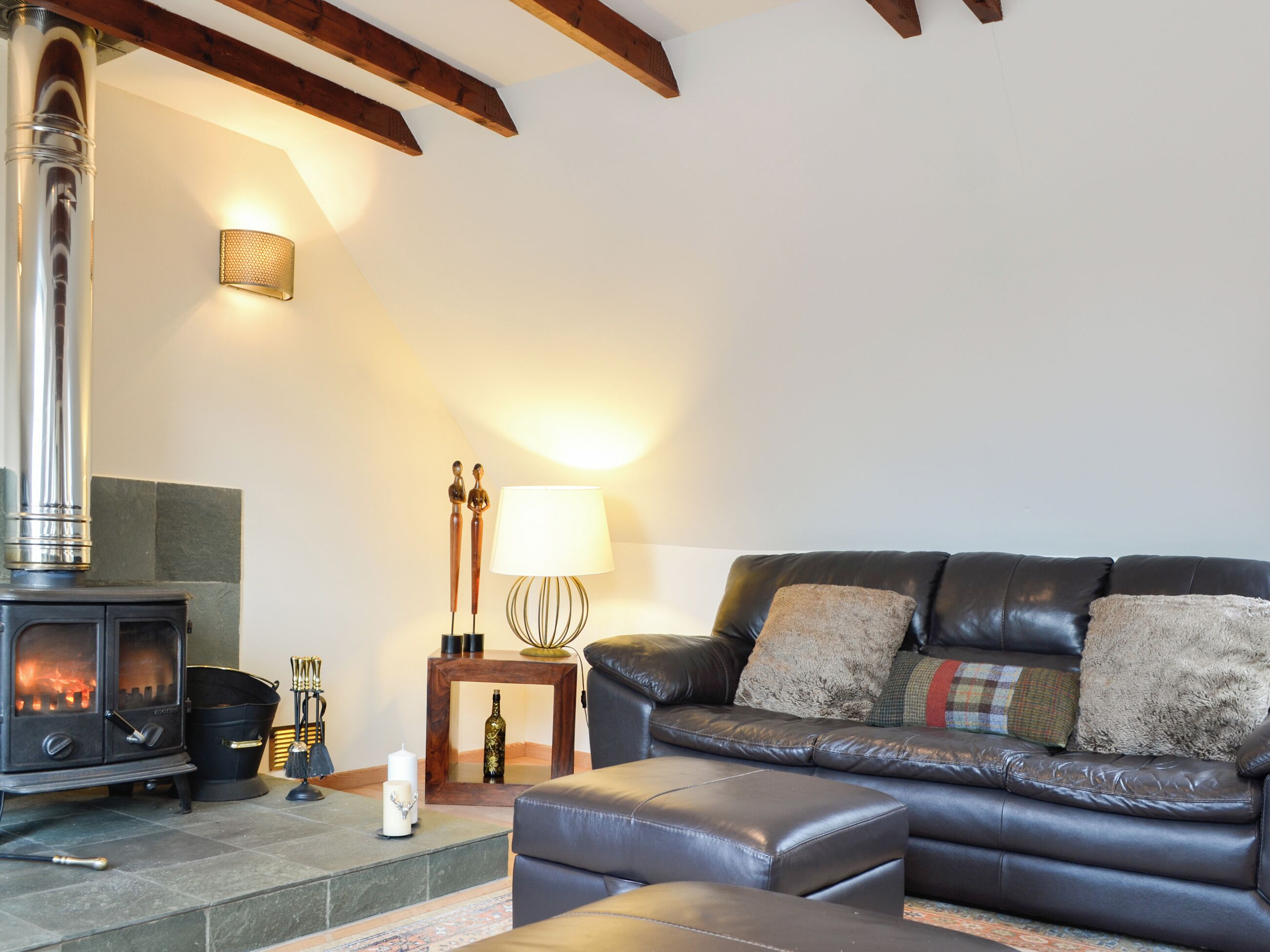 Ein gemütliches Wohnzimmer mit Kamin, Ledersofa und einem kleinen Tisch mit Lampe.