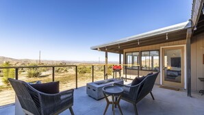 A balcony with wicker furniture, a fire pit, and a view of the desert landscape. - Twilight Terrace - Relax In Style 2 Bedroom Home by RedAwning (Joshua Tree)