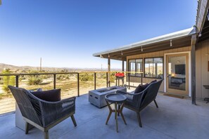 A balcony with wicker furniture, a fire pit, and a view of the desert landscape. - Twilight Terrace - Relax In Style 2 Bedroom Home by RedAwning (Joshua Tree)