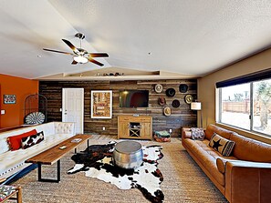 Ein Wohnzimmer mit Kuhfellteppich, Deckenventilator, Fernseher und einer Wand, die mit Hüten geschmückt ist.