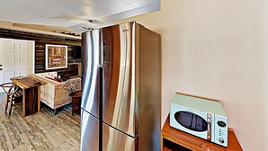 Una cocina con un refrigerador de acero inoxidable, un microondas en un estante de madera y una mesa de comedor con sillas.