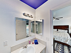 Une salle de bain avec un lavabo blanc, un miroir et un ventilateur de plafond.