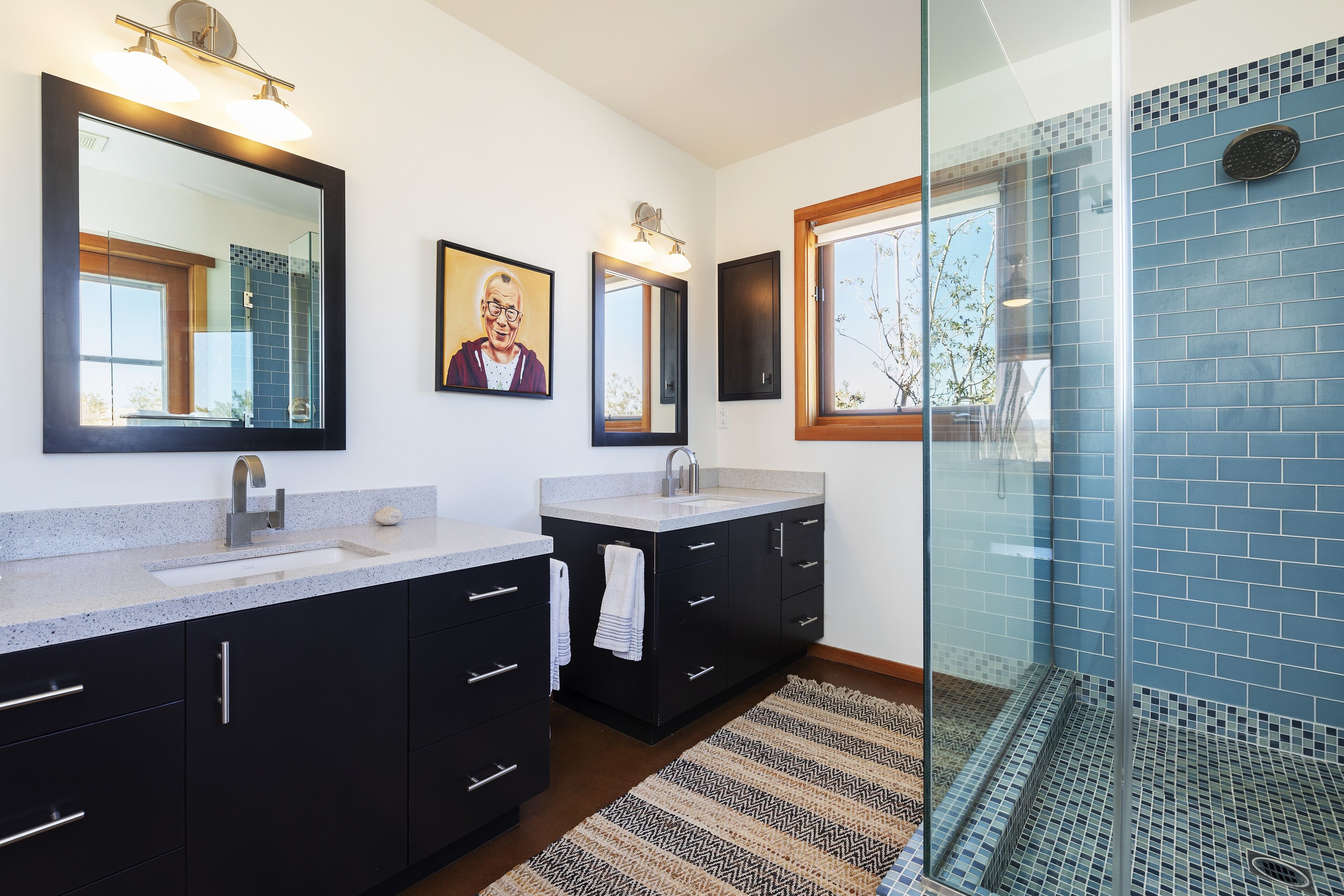 A modern bathroom with two sinks, dark cabinets, and a glass shower enclosure.