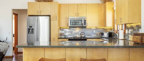Una cocina moderna con armarios de madera, electrodomésticos de acero inoxidable y una isla central con taburetes de bar.