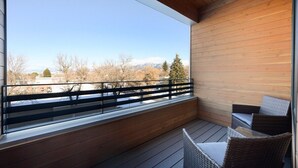 A balcony with a wooden floor, a glass railing, and wicker furniture. - Stylish SOBO Downtown Condo - Steps to Main St. (Bozeman)