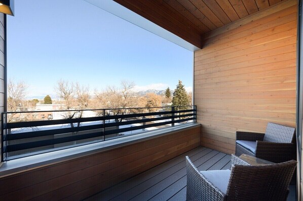 A balcony with a wooden floor, a glass railing, and wicker furniture.