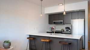 A modern kitchen with a central island, bar stools, a microwave, and a refrigerator. - Stylish SOBO Downtown Condo - Steps to Main St. (Bozeman)