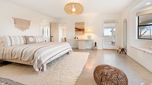 A spacious bedroom with a large bed, a hanging light fixture, a bedside table, and a view through an open door. - Terracasa - Hot Tub, Fire Pit, Outdoor Shower & Endless Views 2 Bedroom Home by RedAwning (Yucca Valley)