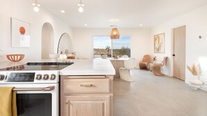 A modern kitchen with a central island, a dining area with a view, and a living space with a sofa and chairs. - Terracasa - Hot Tub, Fire Pit, Outdoor Shower & Endless Views 2 Bedroom Home by RedAwning (Yucca Valley)