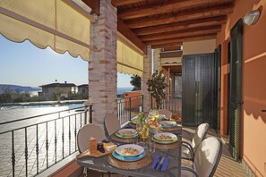 An outdoor dining area with a table set for four, overlooking a body of water. - Le Terrazze PT 31 by Wonderful Italy (Toscolano Maderno)
