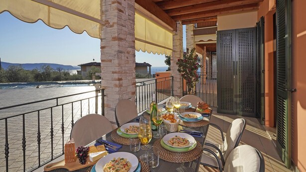 A balcony with a table set for a meal, overlooking a body of water and mountains. - Le Terrazze PT 31 by Wonderful Italy (Toscolano Maderno)