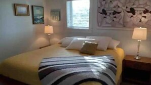 A neatly arranged bedroom with a bed, two bedside lamps, and a window with blinds. - Eagle Pass Cabina- Unique Cabin Perfect for Two! (Hatteras)