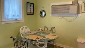 A dining area with a glass table, white chairs, a small decorative item, and an air conditioning unit mounted on the wall. - Eagle Pass Cabina- Unique Cabin Perfect for Two! (Hatteras)