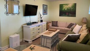 A living room with a flat-screen TV, a ceiling fan, a painting, and a green sofa. - Eagle Pass Cabina- Unique Cabin Perfect for Two! (Hatteras)