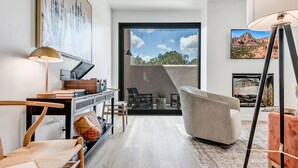 Una sala de estar moderna con un sofá, un escritorio con lámpara, una chimenea y un ventanal con vistas al exterior.