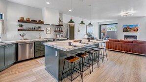 Una cocina moderna con una isla central, taburetes de bar y un comedor con sofá.