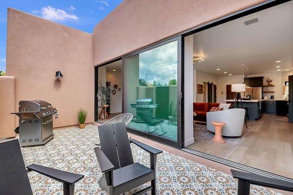 A modern outdoor patio with a grill, seating, and a view into the living area.