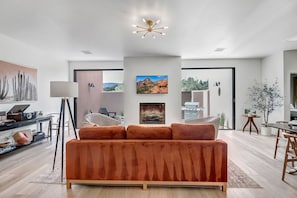 A modern living room with a large orange sofa, a fireplace, and a ceiling light fixture.