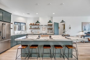 A modern kitchen with a large island, bar stools, and pendant lighting.