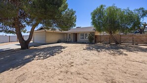A house with a garage, a driveway, and a sandy yard. - Cosmic Rabbit - Family Fun With Hot Tub!! 3 Bedroom Home by RedAwning (Joshua Tree)
