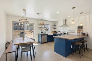 A modern kitchen with a large island, bar stools, and a dining area with a bench and chairs. - Cosmic Rabbit - Family Fun With Hot Tub!! 3 Bedroom Home by RedAwning (Joshua Tree)
