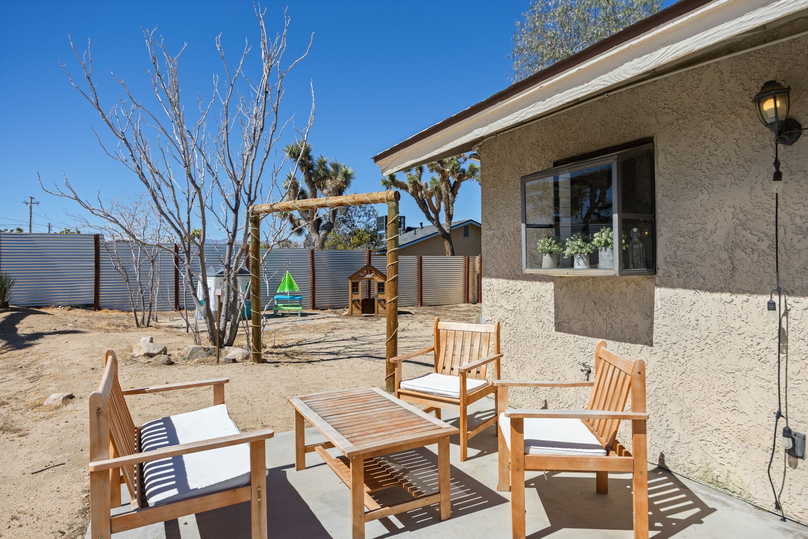 Un patio con muebles de madera, una pérgola y una casa con ventana.