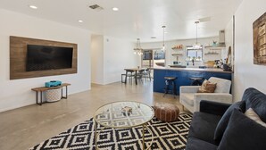 A modern living room with a glass coffee table, a sofa, and a TV mounted on the wall. - Cosmic Rabbit - Family Fun With Hot Tub!! 3 Bedroom Home by RedAwning (Joshua Tree)