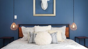 A bedroom with a blue wall, a wooden headboard, patterned pillows, a fluffy white pillow, and two pendant lights. - Cosmic Rabbit - Family Fun With Hot Tub!! 3 Bedroom Home by RedAwning (Joshua Tree)