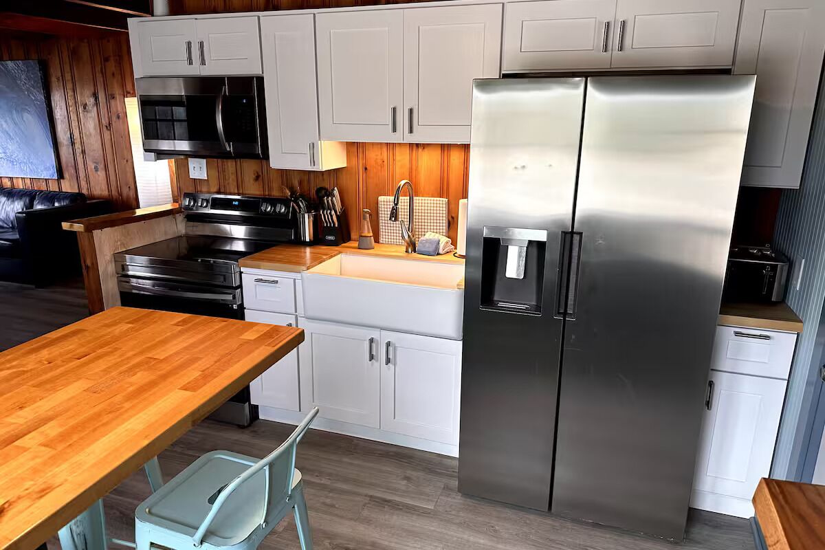 A modern kitchen with white cabinets, stainless steel appliances, and a wooden table.