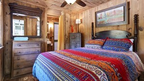Ein Schlafzimmer mit Holzwandverkleidung, einem Bett, einem Schminktisch und einem Deckenventilator.