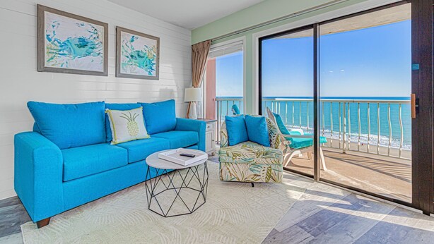 A room with a blue sofa, a patterned armchair, and a view of the ocean through large sliding glass doors.