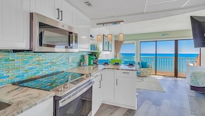 A modern kitchen with a large island, white cabinetry, and a view of the ocean through the sliding glass doors.