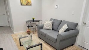 A living room with a grey sofa, two patterned cushions, a glass coffee table, and a small round table with chairs. - Grande Royale (Saskatoon)