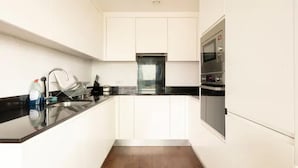 A modern kitchen with white cabinets, a black countertop, and stainless steel appliances including a microwave and oven. - Remarkable 2-bed Apartment in London Amazing Views (London)