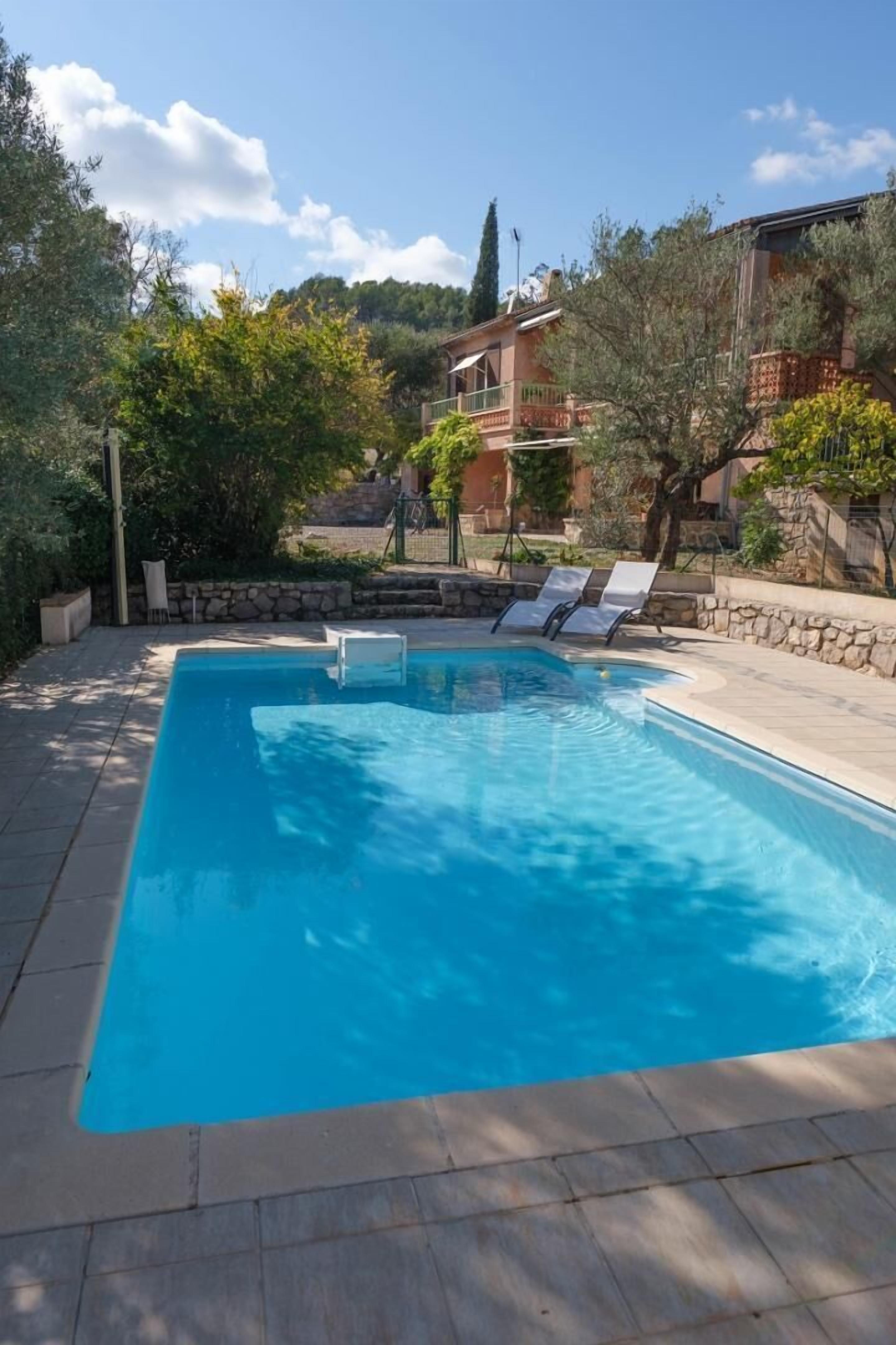 A rectangular swimming pool with clear blue water, surrounded by a stone wall and a tiled deck. There are lounge chairs along the poolside.