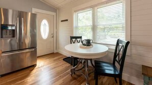 A kitchen with a stainless steel refrigerator, a white door, and a window with blinds.