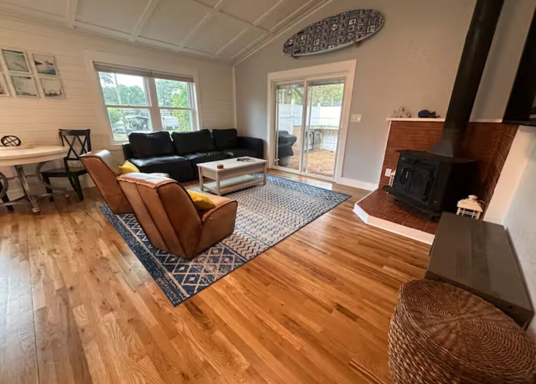 Ein geräumiges Wohnzimmer mit Kamin, einer schwarzen Ledersofa, einem Holztisch und einem gemusterten Teppich.