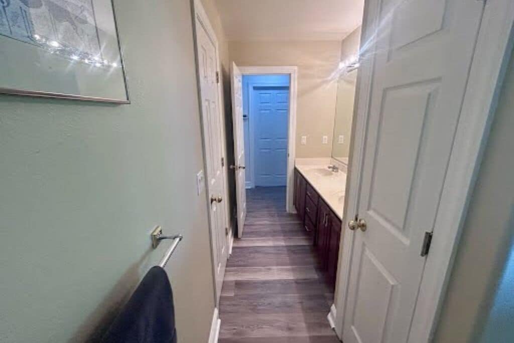 A narrow hallway with a door at the end, a towel rack on the left, and a sink with cabinets on the right.