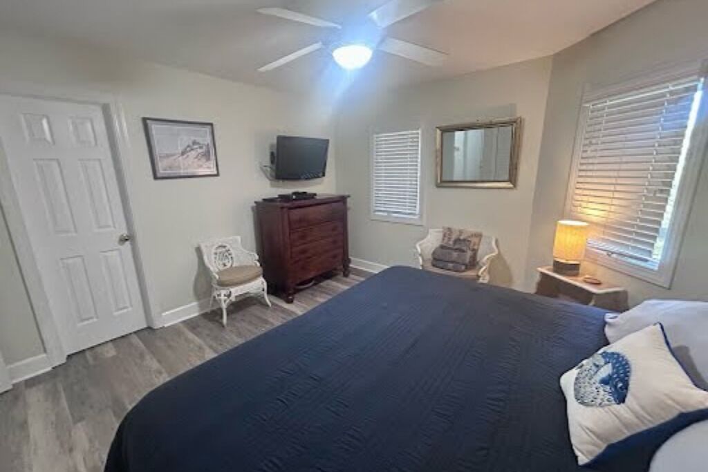A bedroom with a bed, dresser, TV, chair, and window with blinds.