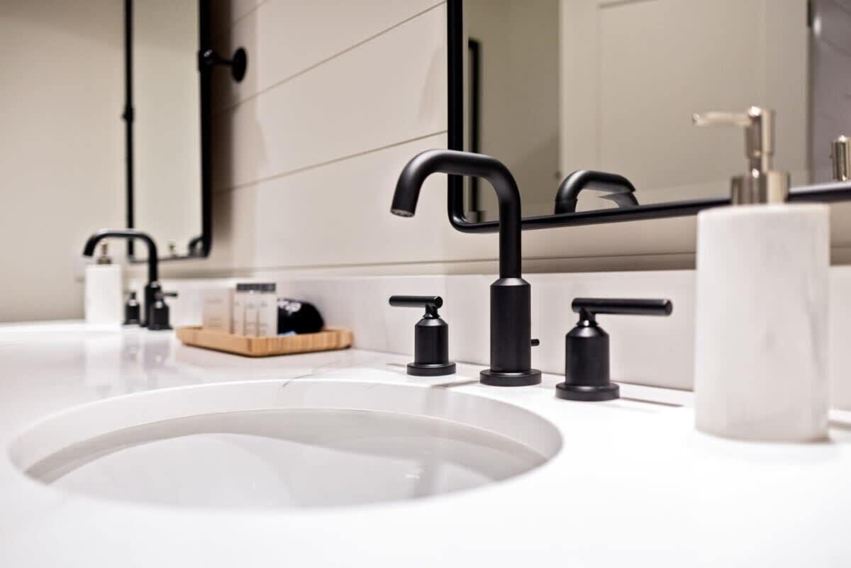 Un bany modern amb un lavabo blanc, aixetes negres i un mirall gran.