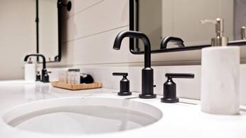 Un bany modern amb un lavabo blanc, aixetes negres i un mirall gran.