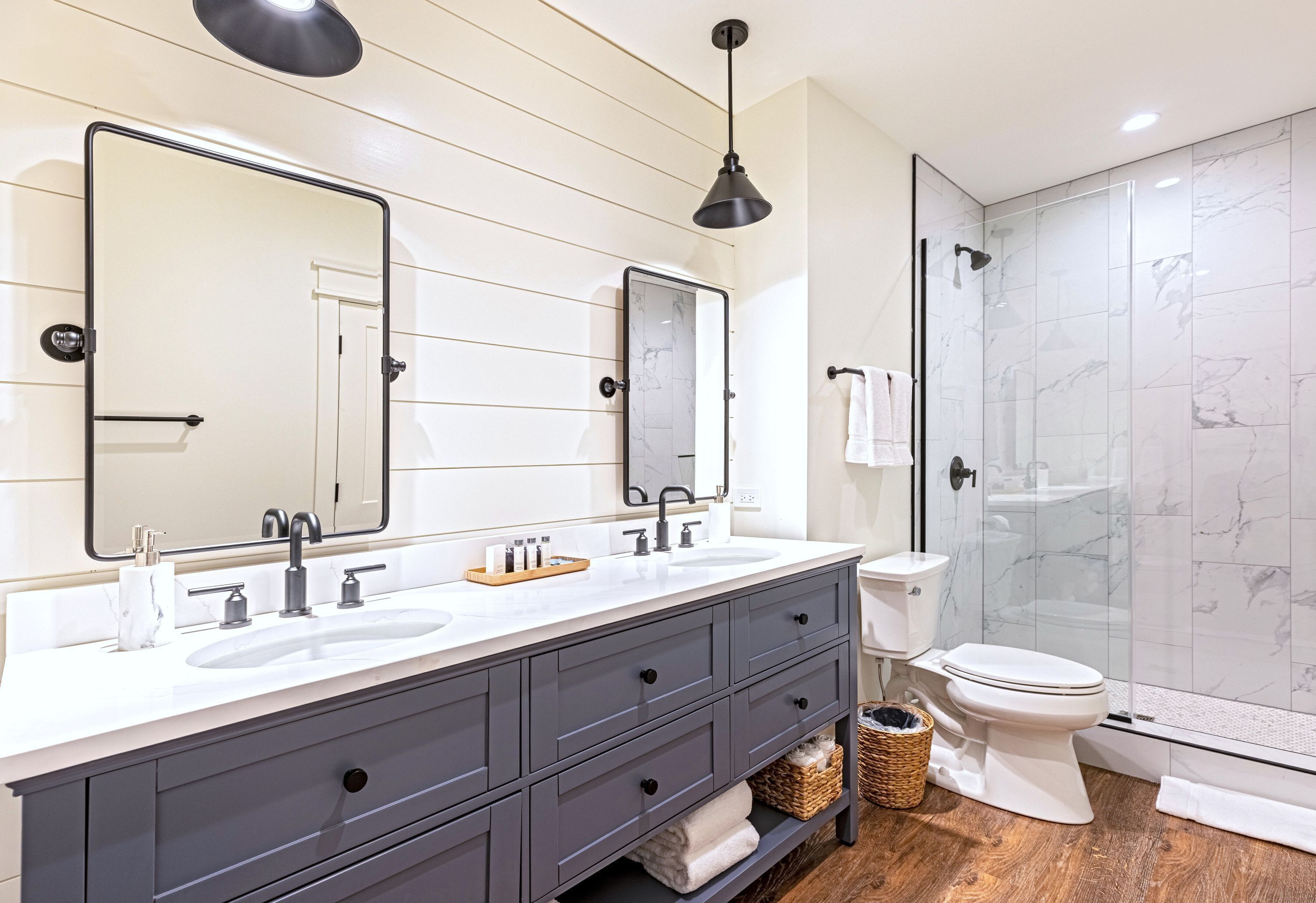 A bathroom with a double sink vanity, a large mirror, a glass shower enclosure, and a toilet.