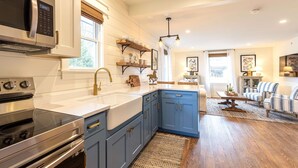 A modern kitchen with stainless steel appliances, blue cabinets, and a dining area with striped chairs. - Kildahl House - Boutique Farmhouse Suite #3 (West Dundee)