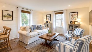 A living room with a white sofa, striped armchair, wooden dining table, and a coffee table with decorative items. - Kildahl House - Boutique Farmhouse Suite #3 (West Dundee)
